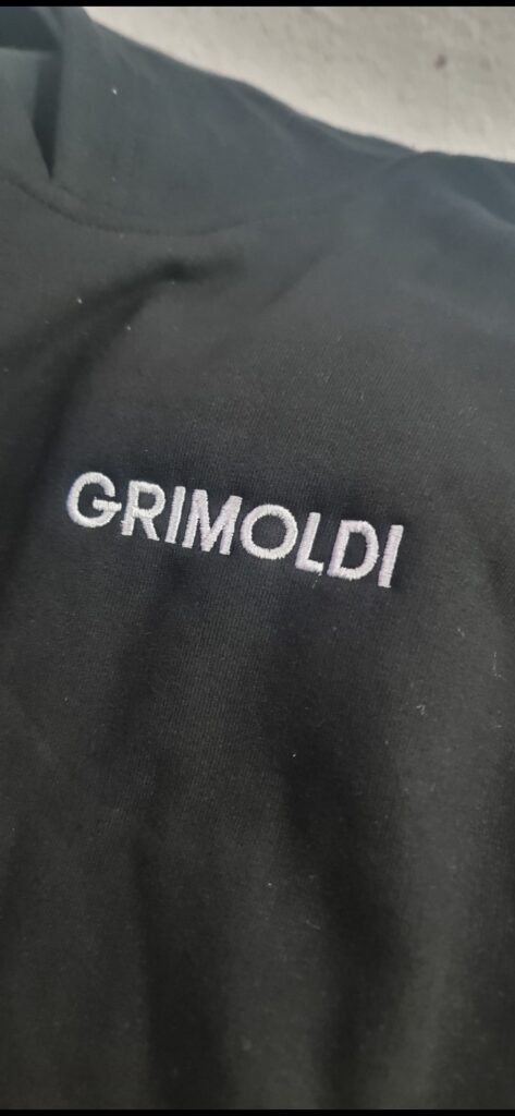 Bordado computarizado del logo Grimoldi en hilo blanco sobre prenda negra