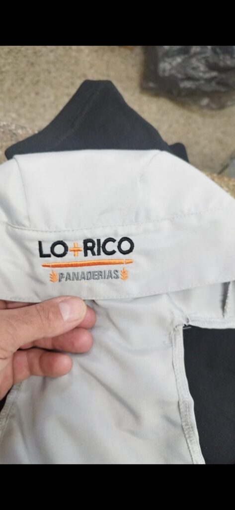 Bordado industrial del logo Lo Rico Panaderías en hilo negro y naranja sobre camisa gris