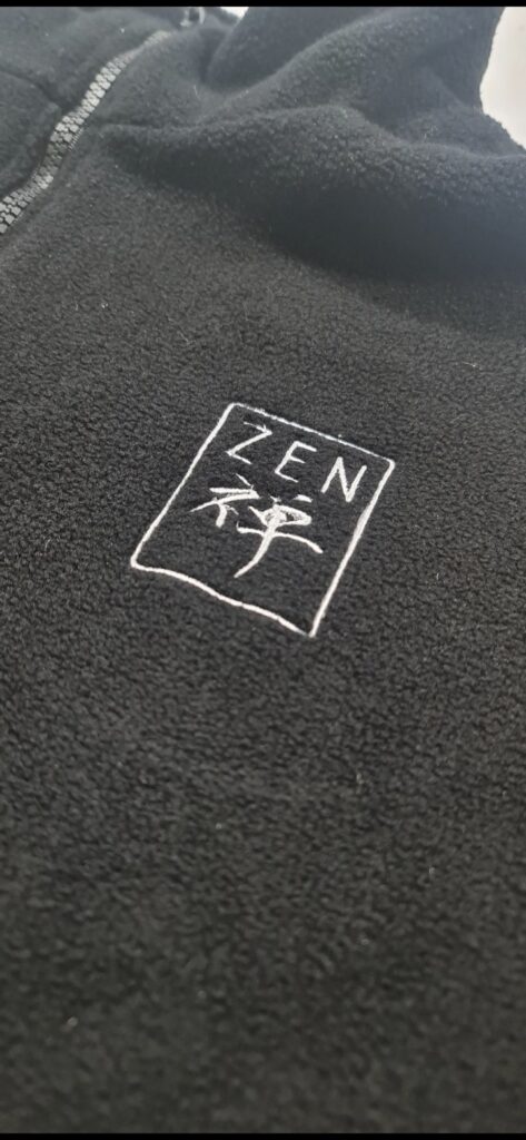 Bordado computarizado del logo ZEN en hilo blanco sobre buzo de polar negro